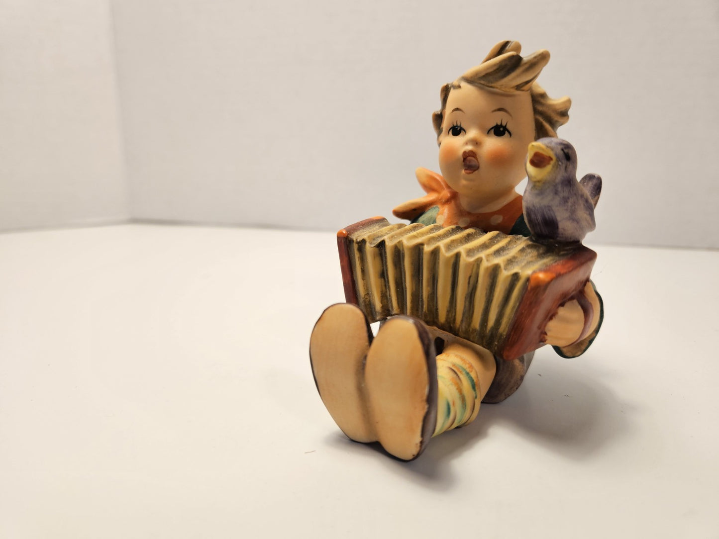 Vintage-style figurine of a child playing an accordion with a bird on a white background music