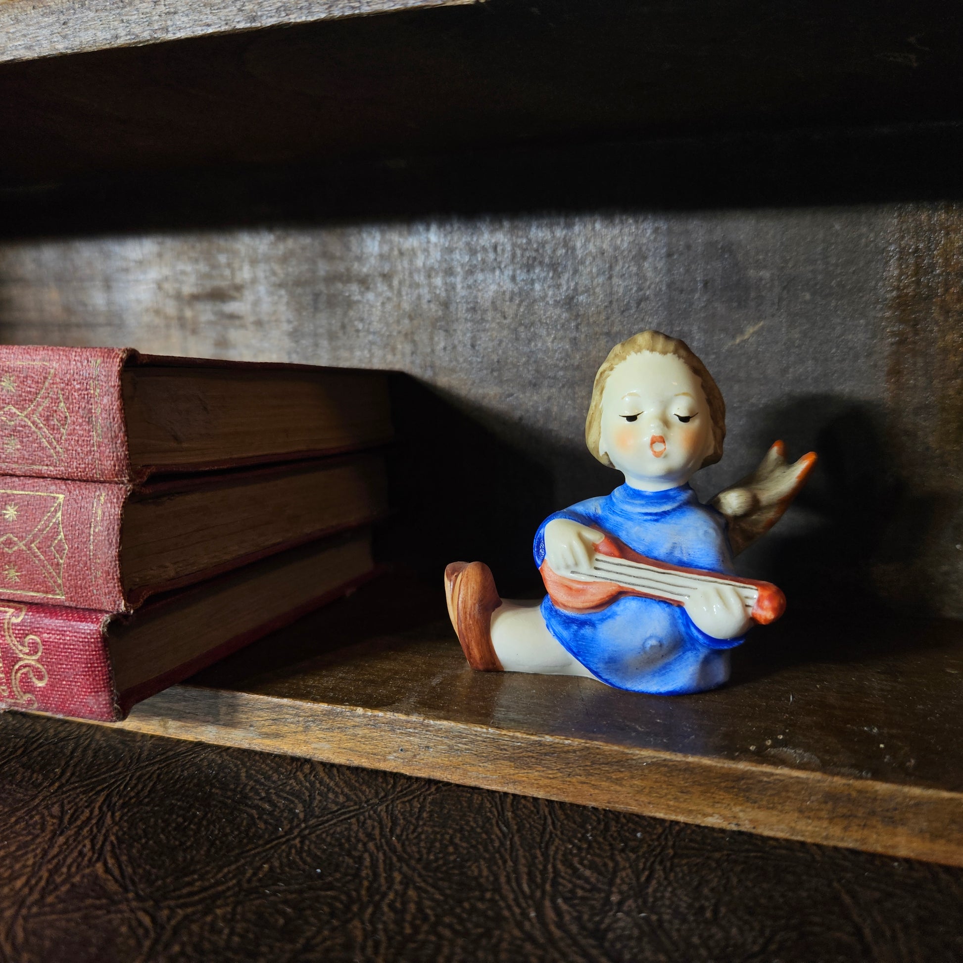 Small figurine of a girl angel playing a lute on a wooden shelf with an open book.