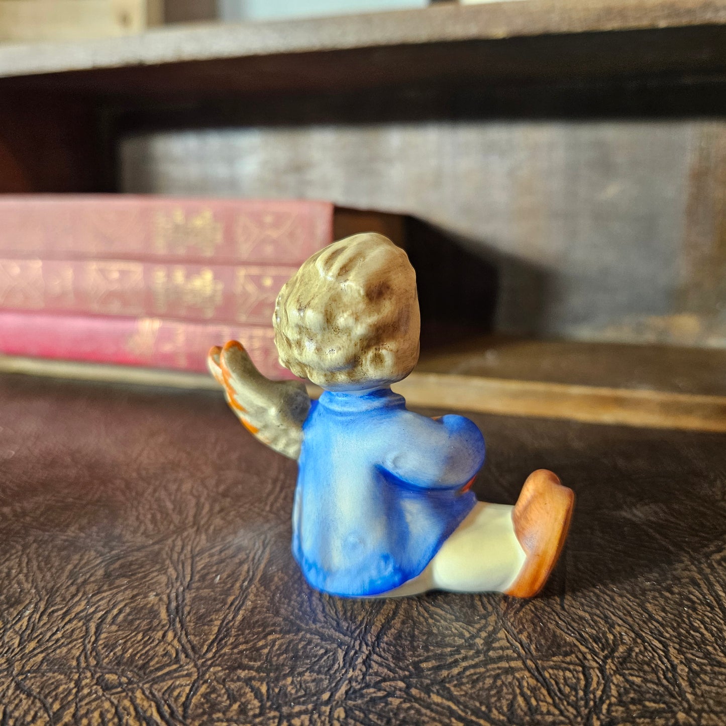 Small figurine of a child  angel sitting on a textured surface with books in the background