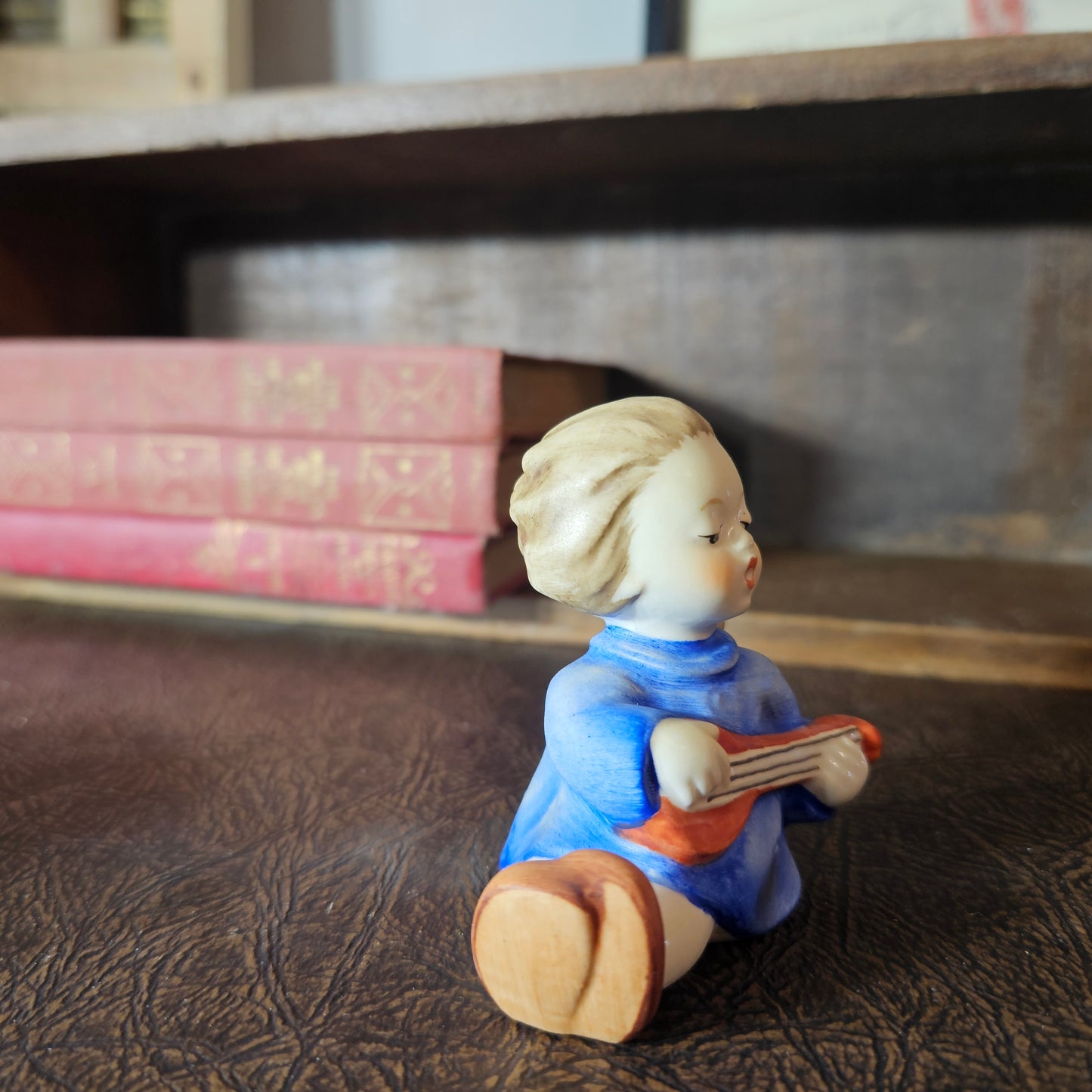 Small figurine of a angel playing a guitar on a textured surface with books in the background.