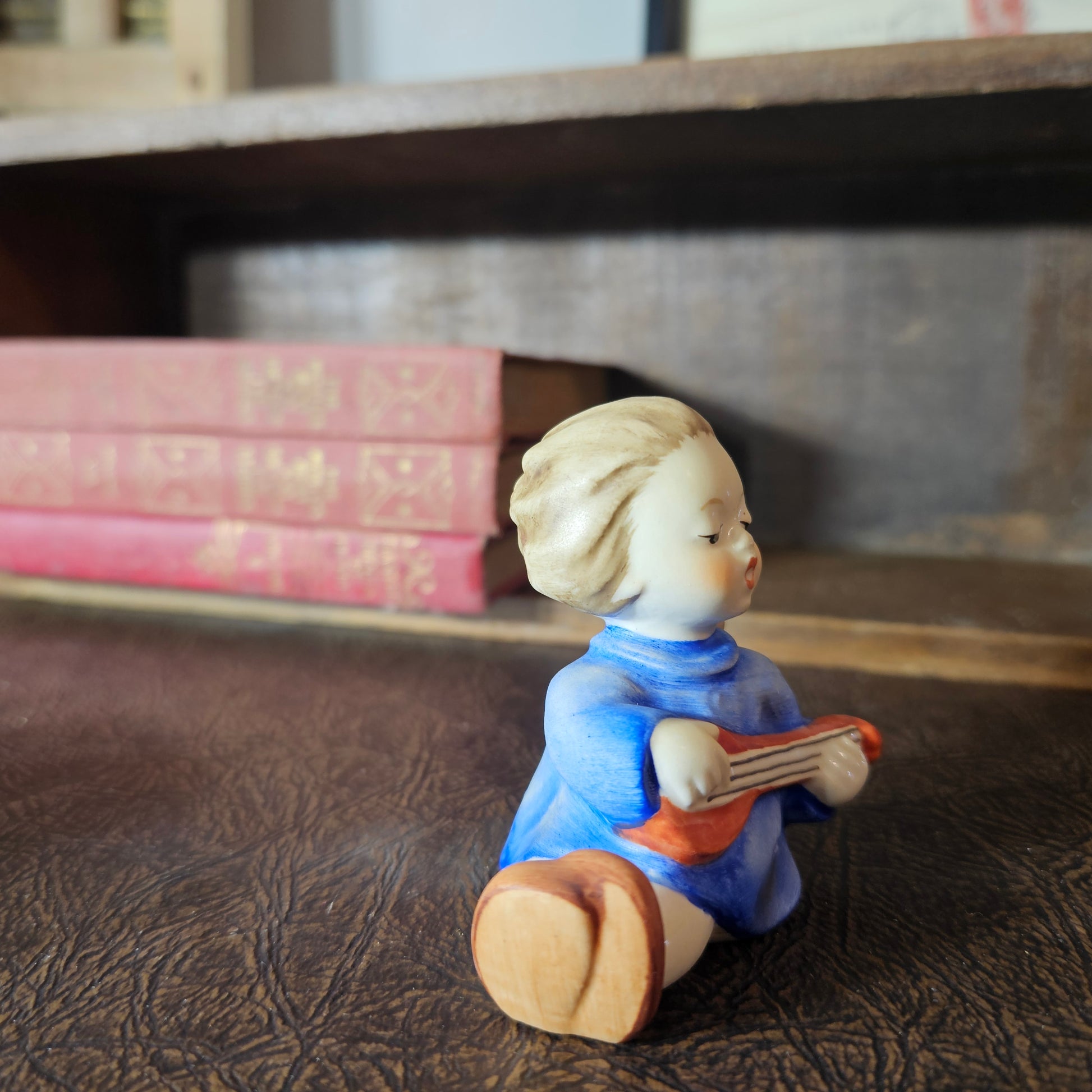 Small figurine of a angel playing a guitar on a textured surface with books in the background.