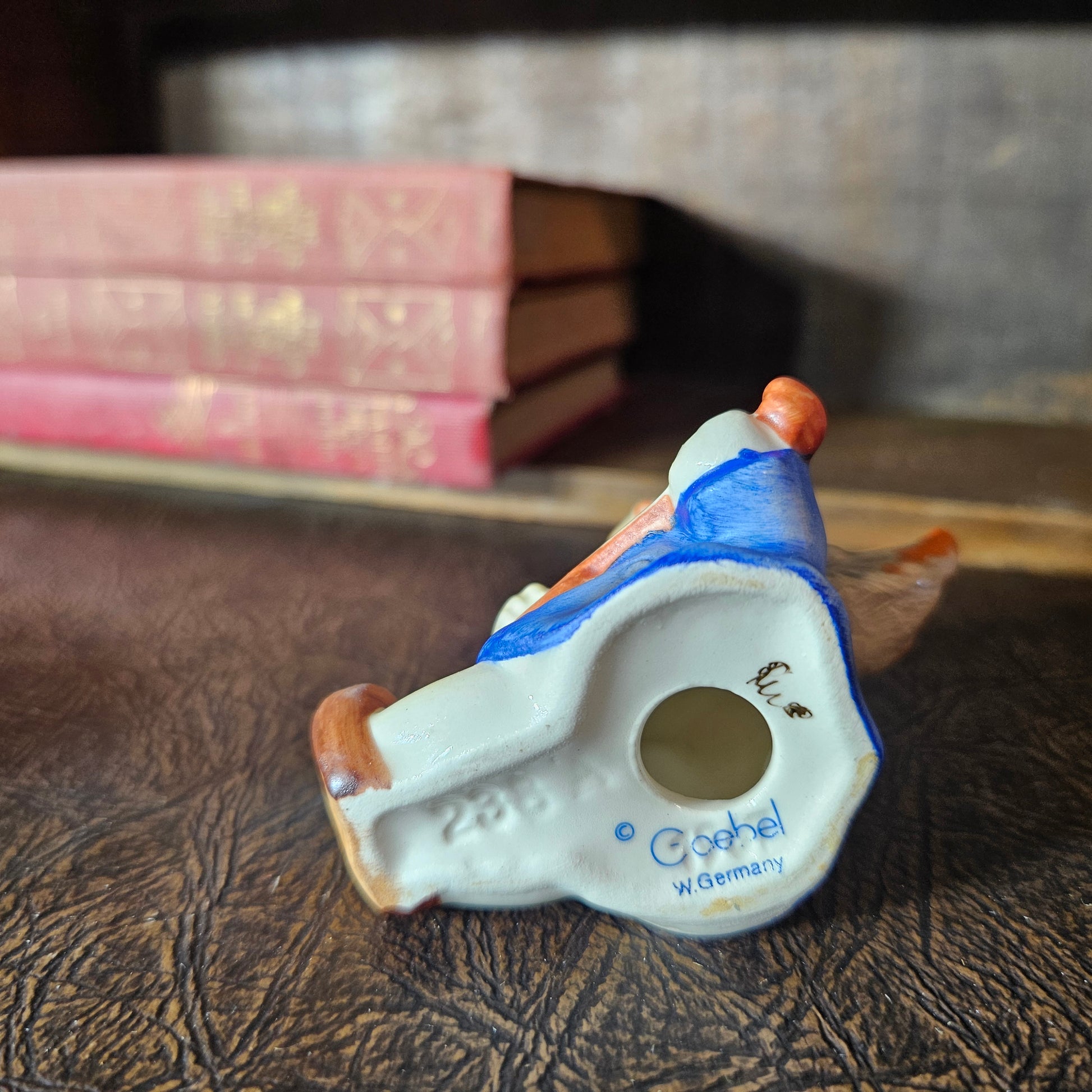 Decorative ceramic piece with 'Goebel' branding on a textured surface with books in the background