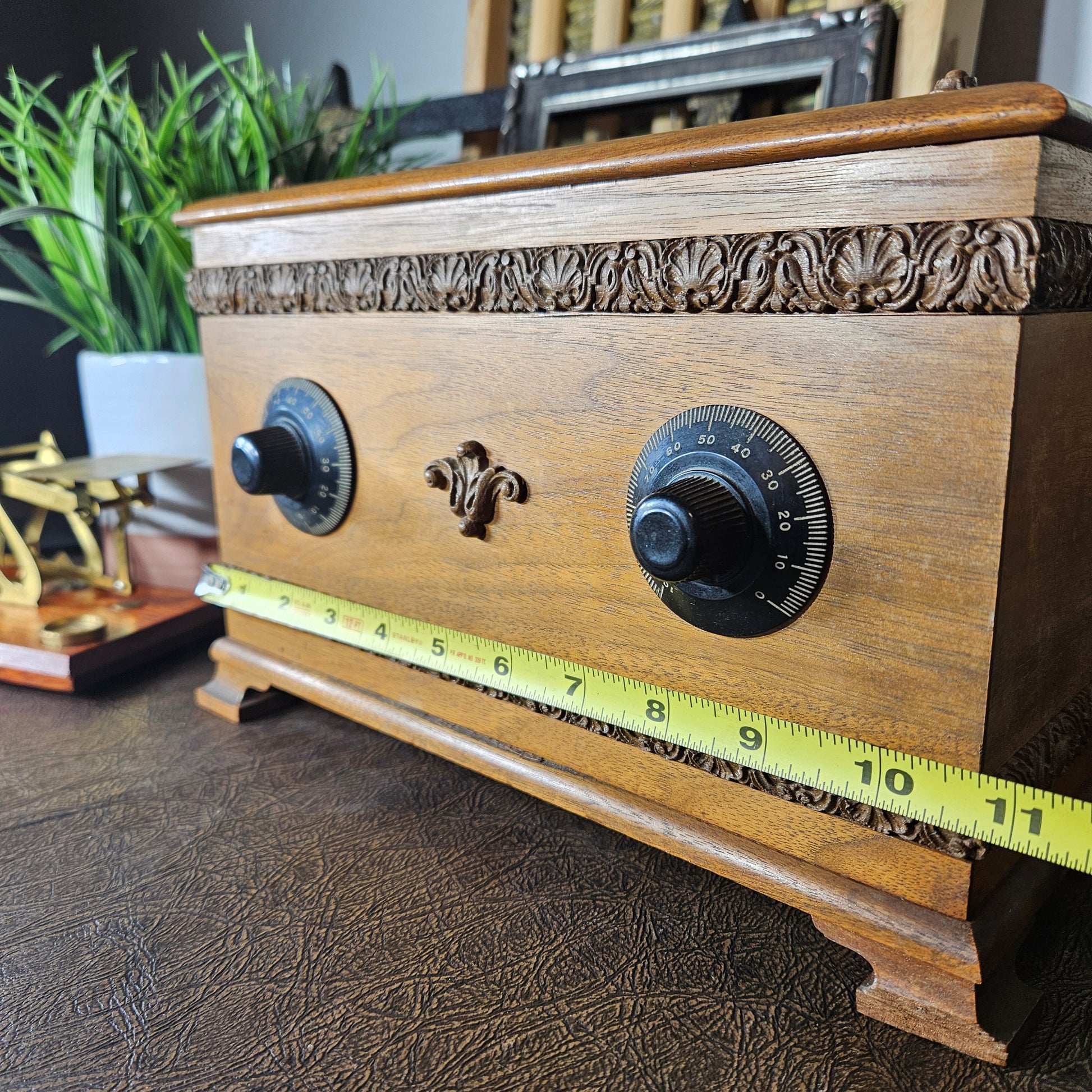 Wooden radio music box with decorative carvings and a tape measure for scale on a textured surface.