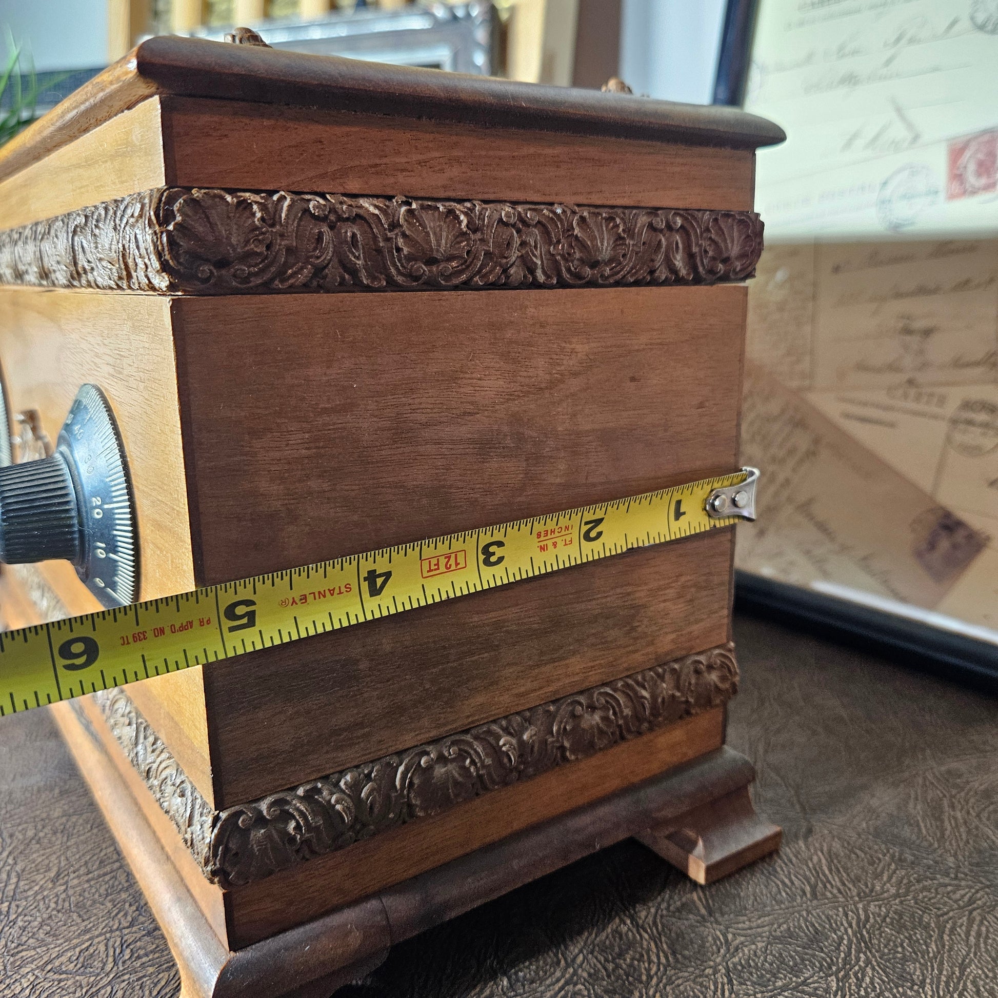 Wooden music box with intricate carvings and a measuring tape for scale.