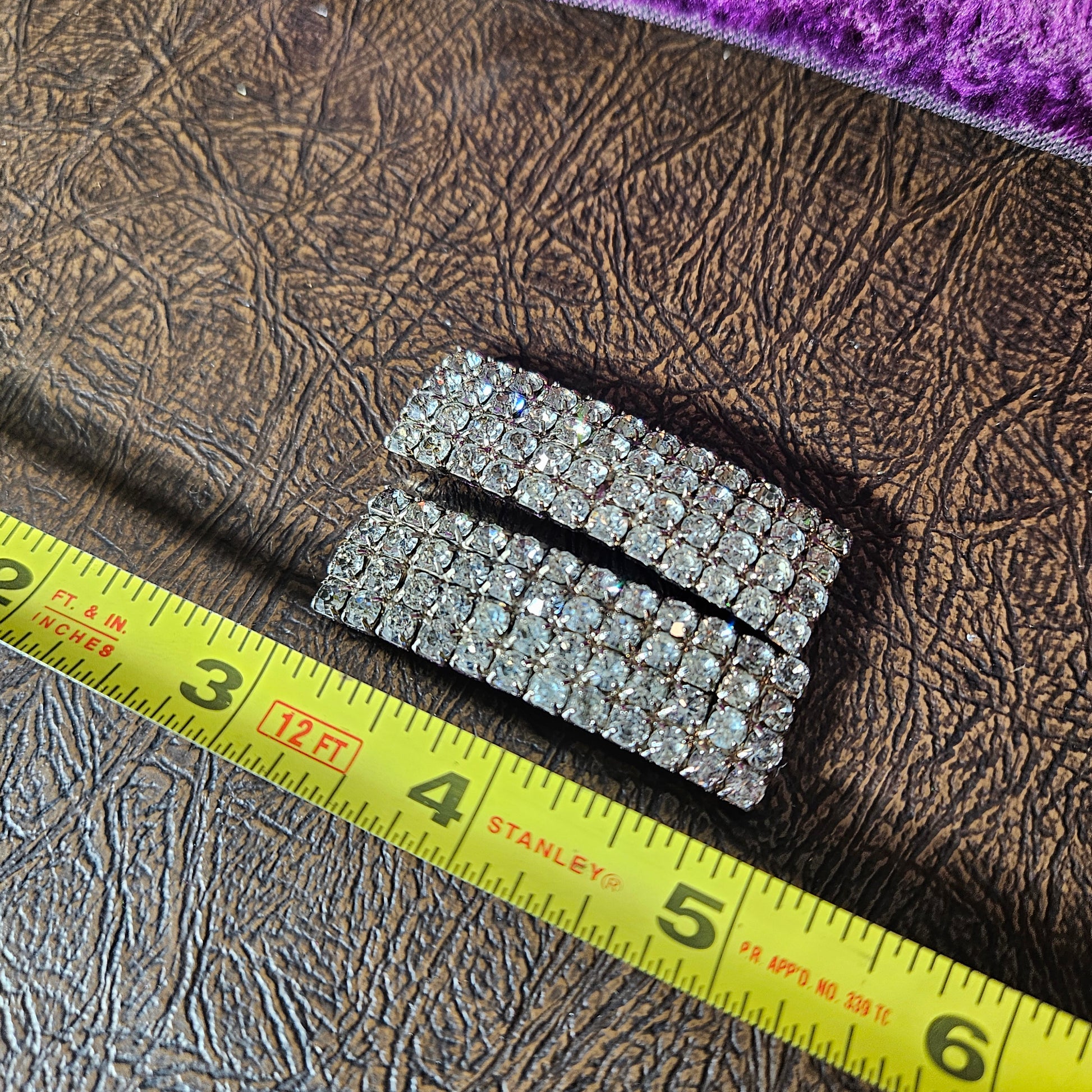 Silver rhinestone belt buckle with a measuring tape for scale on a textured surface