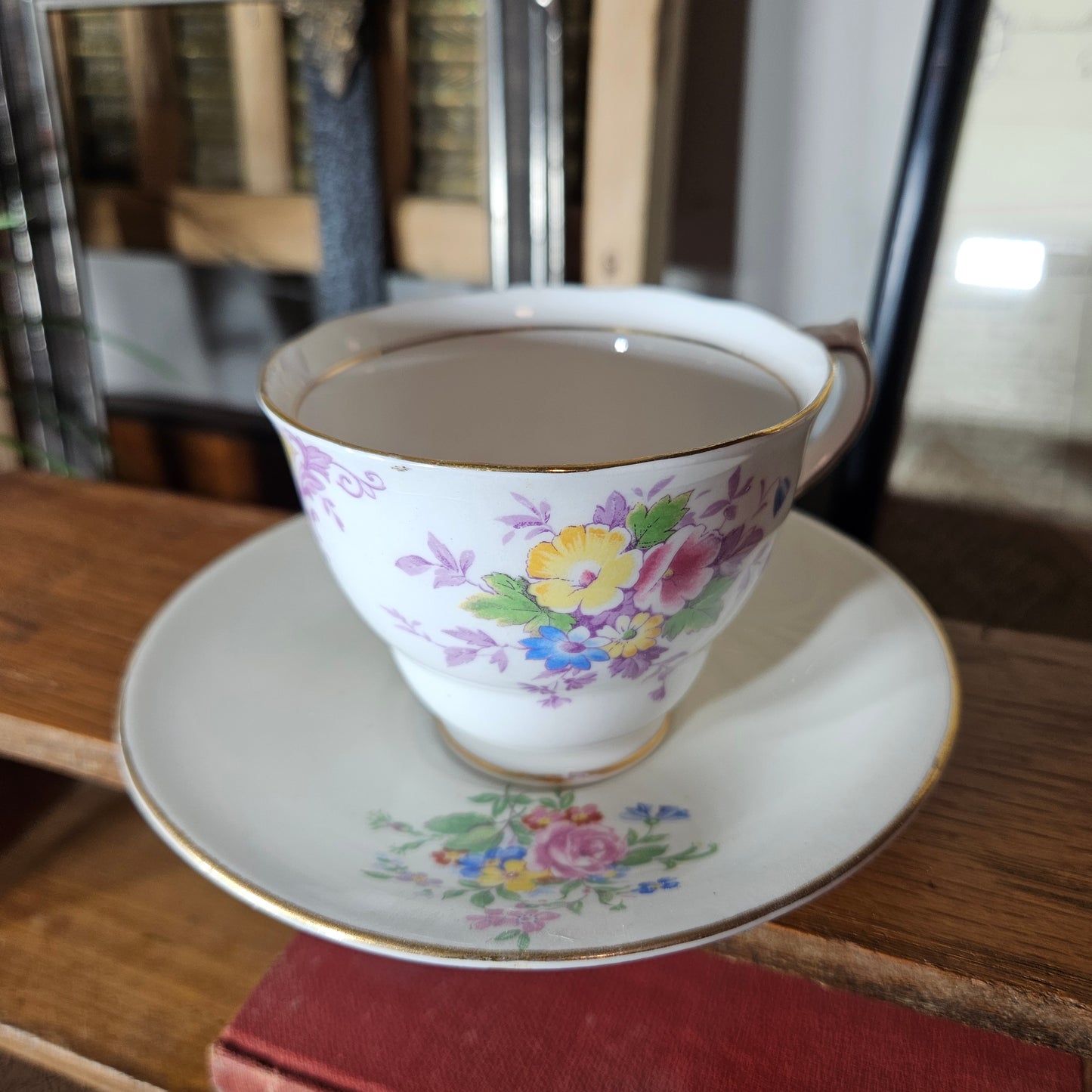 Floral-patterned teacup and saucer on a wooden surface with books in the background