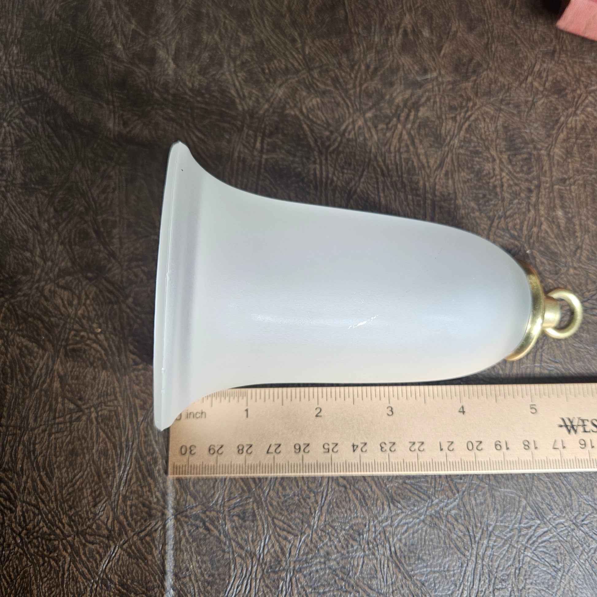 White lampshade with gold fixture on a textured surface next to a ruler for scale.