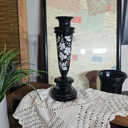 Decorative black candlestick with white floral patterns on a textured surface.