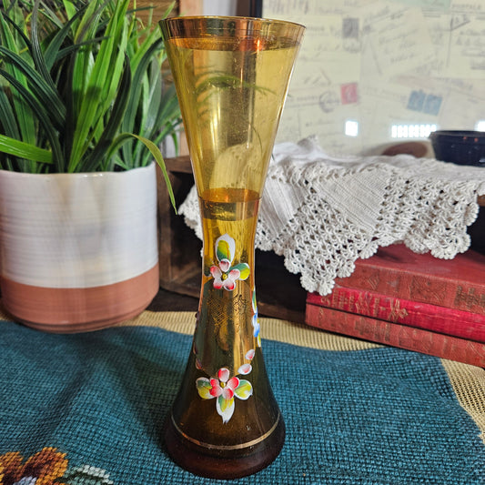 Decorative glass vase with floral designs on a table with a plant and books in the background.