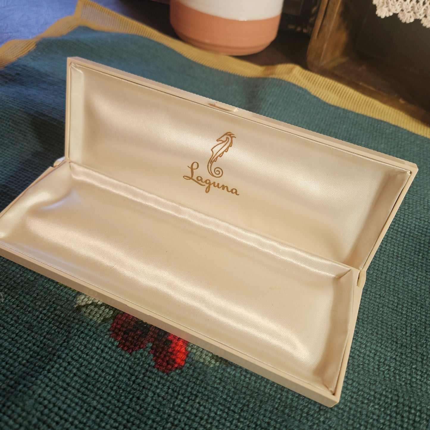 Beige pouch with 'Laguna' branding on a textured green surface