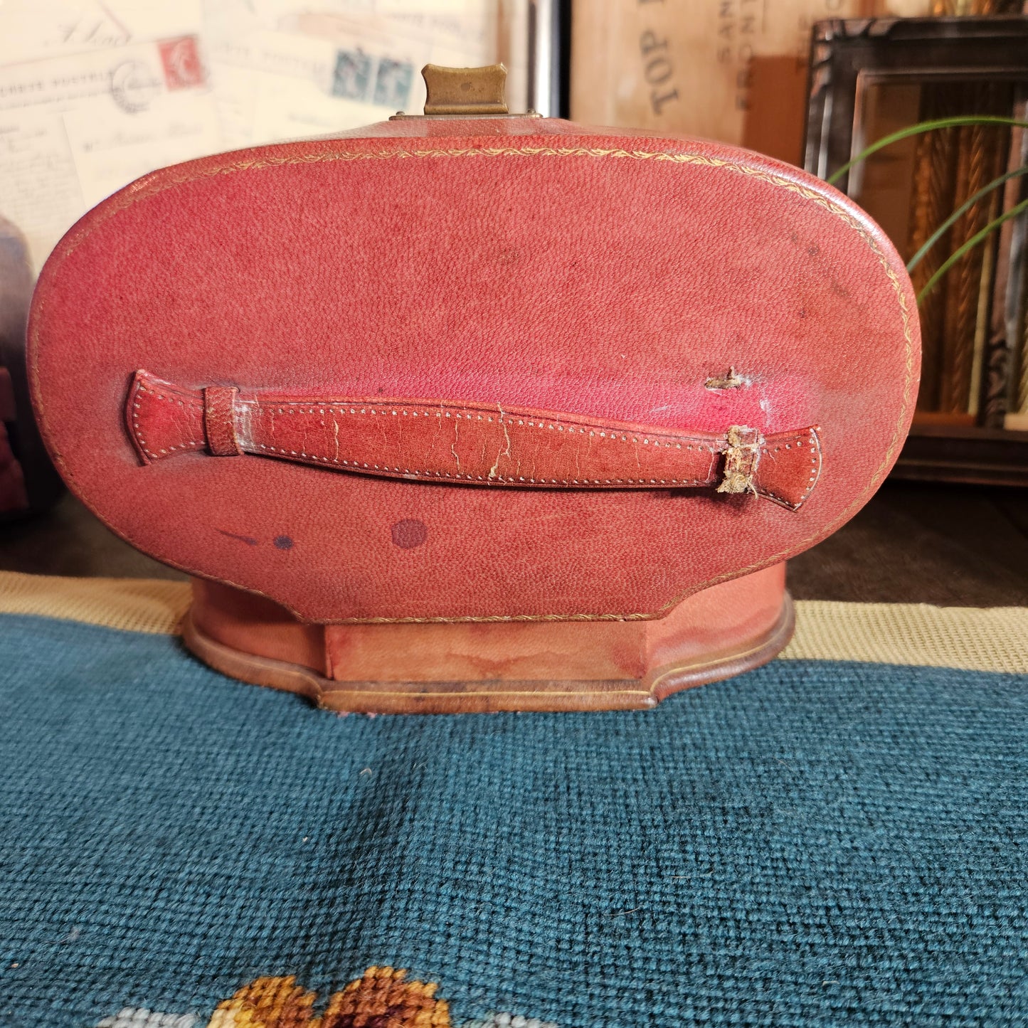 Vintage red leather suitcase on a textured surface with books and papers in the background