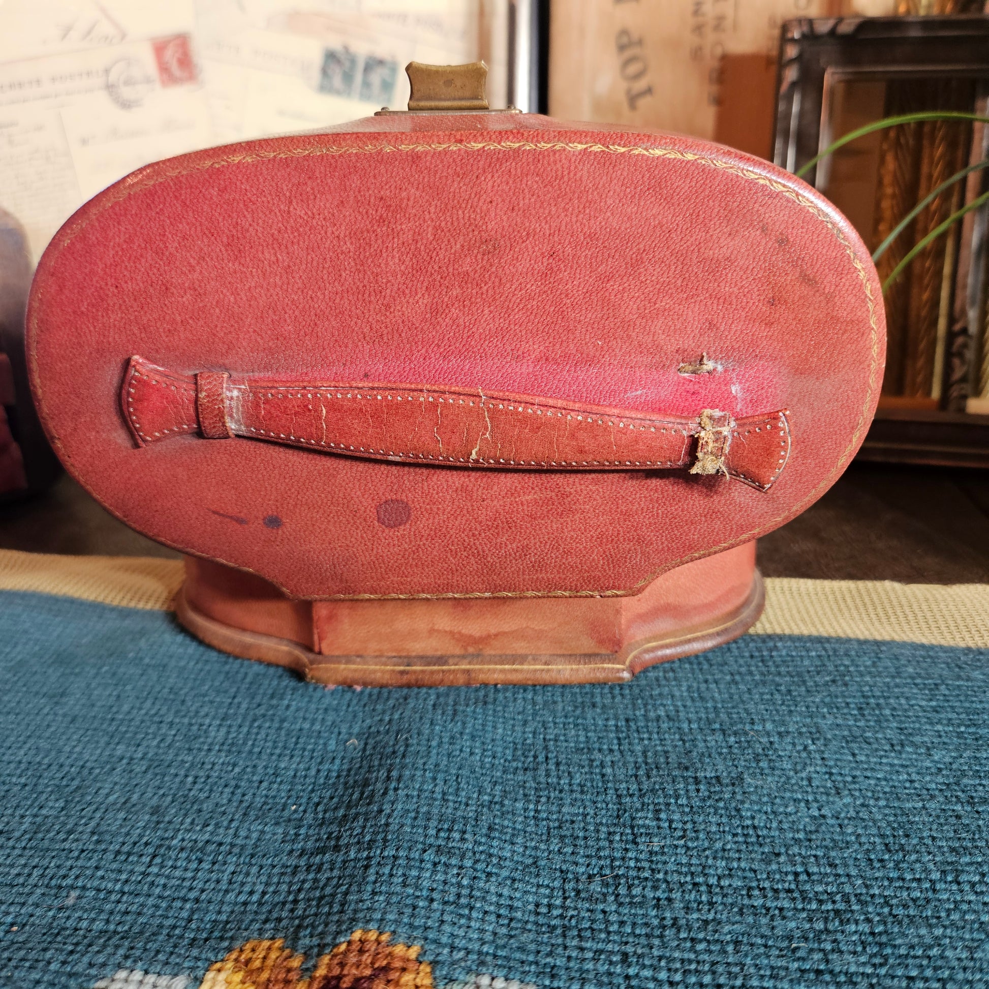 Vintage red leather suitcase on a textured surface with books and papers in the background