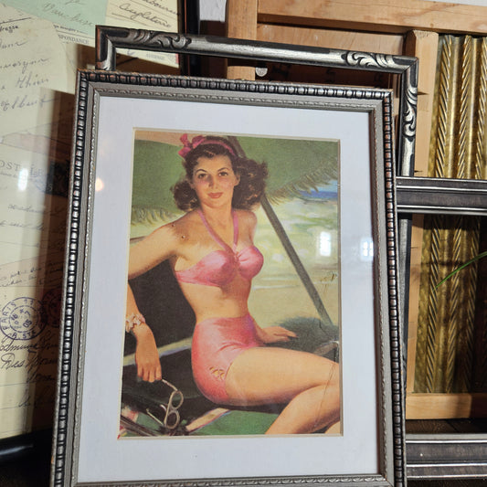 Framed vintage-style poster of a woman in a pink swimsuit on a wooden surface.