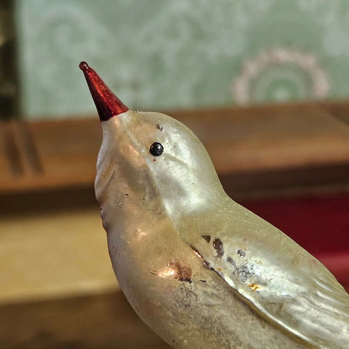 A close-up of a metallic bird figurine with a silver body and a pointed red beak, set against a blurred background.