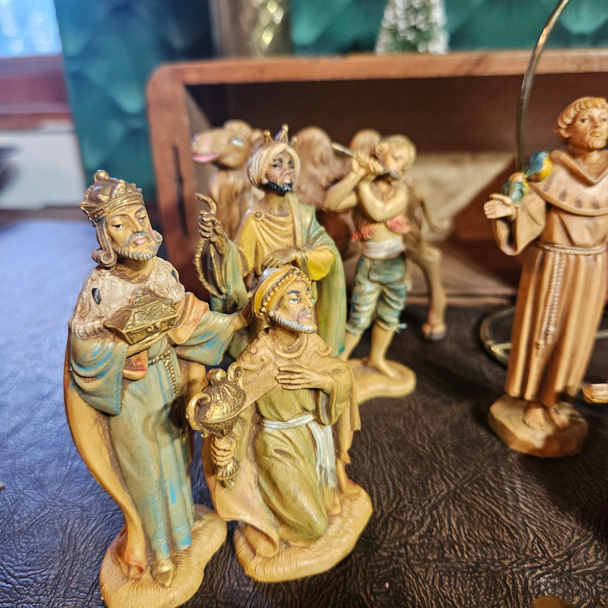 A small set of hand-painted nativity figurines displayed on a dark textured surface, with a wooden shelf in the background.