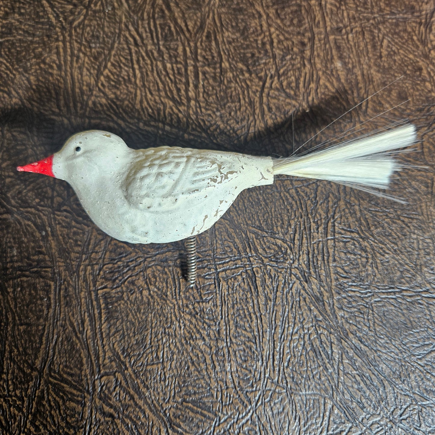 White bird-shaped object with a red beak on a textured brown surface