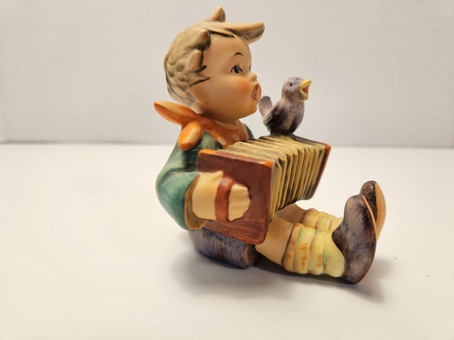 Vintage-style figurine of a boy playing an accordion with a bird on his shoulder against a plain background.