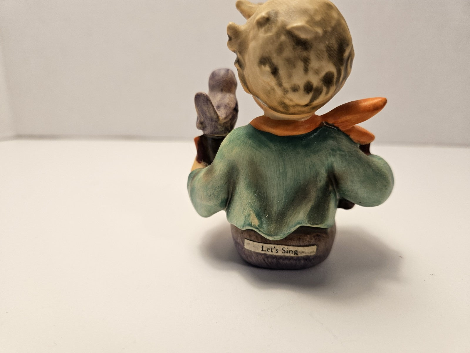 Small figurine of a character with a green shirt and brown hat on a white background "let's sing"