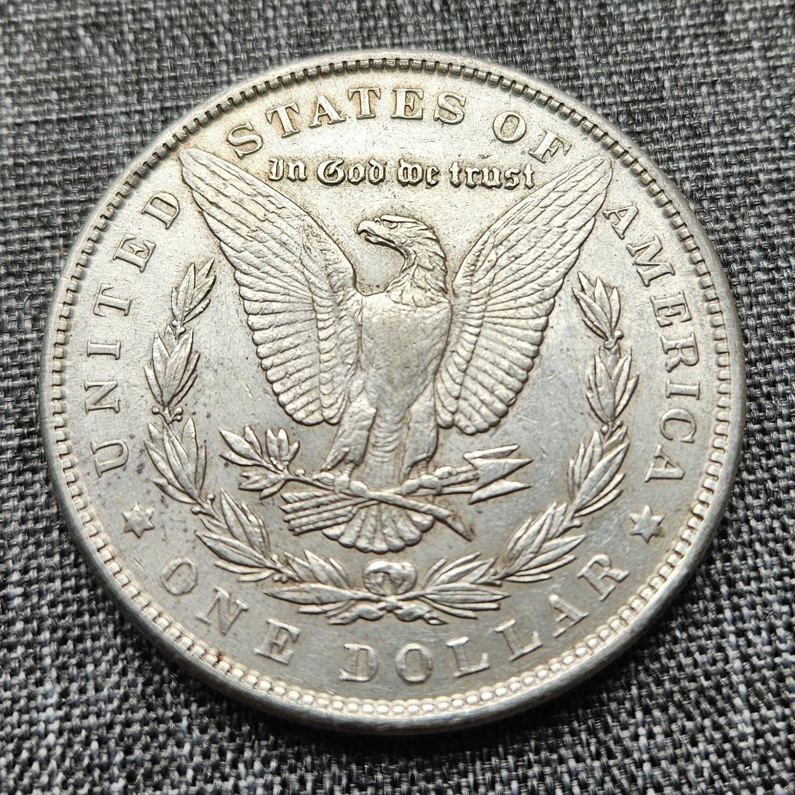 Silver dollar coin with an eagle design on a textured gray fabric background
