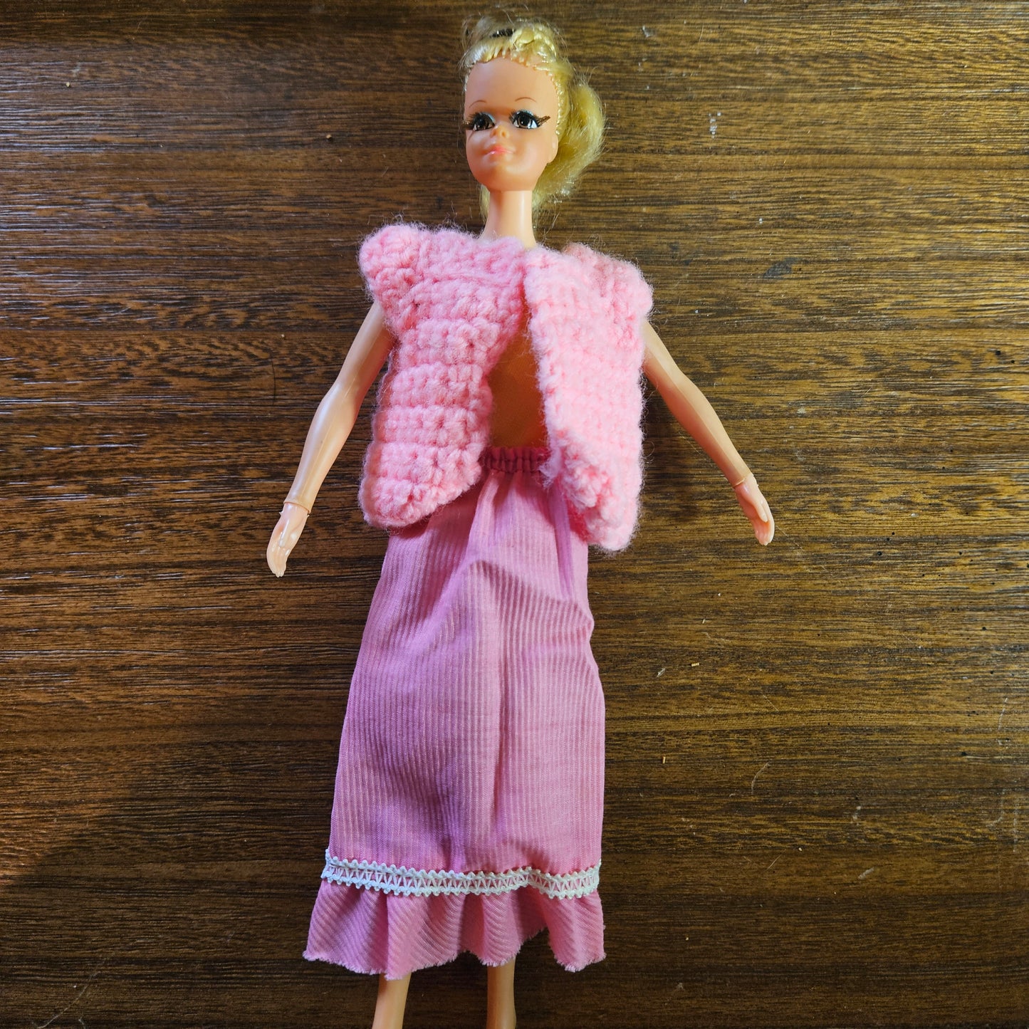 Barbie doll wearing a pink dress and matching vest on a wooden surface